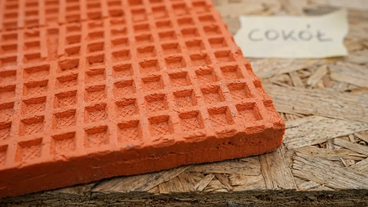 Zbliżenie na waflową strukturę powierzchni pomarańczowej płyty XPS do izolacji cokołu, leżącej na płycie OSB.